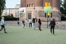 Pictured is a group of youths playing basketball at an outdoor basketball field. The hoops was designed through the Equalizer project, with hoops on both sides of the pole.