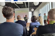 Photo of people in an audience listening to a presenter. At the top is the Share-north logo and the EU-flag.
