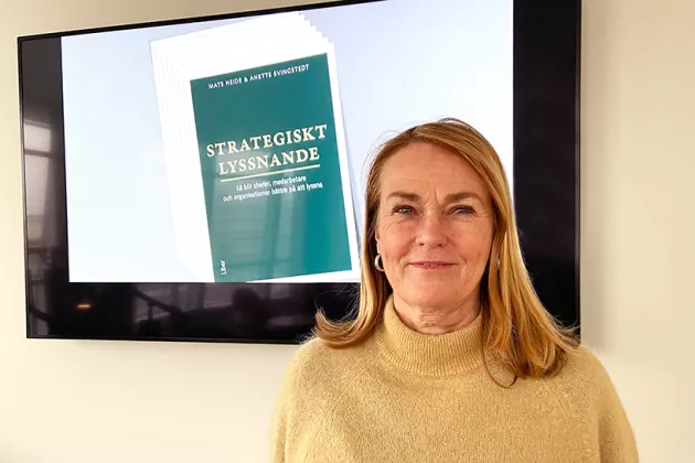 Anette Svingstedt framför en TV-skärm med bild på bokomslag "Strategiskt lyssnande". Foto.