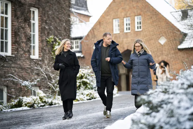 Tre medelålders personer går utomhus och pratar med varandra.