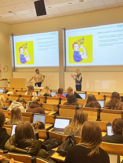 Foto på föreläsningssal, längst fram står två kvinnor och pratar