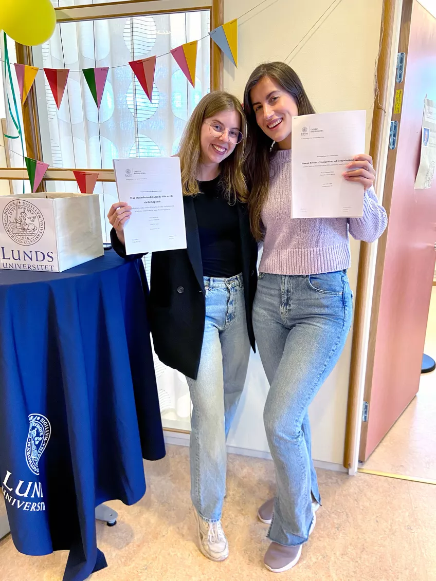 Emilia Björklund och Alexandra Lemvall håller upp sina examensarbeten.