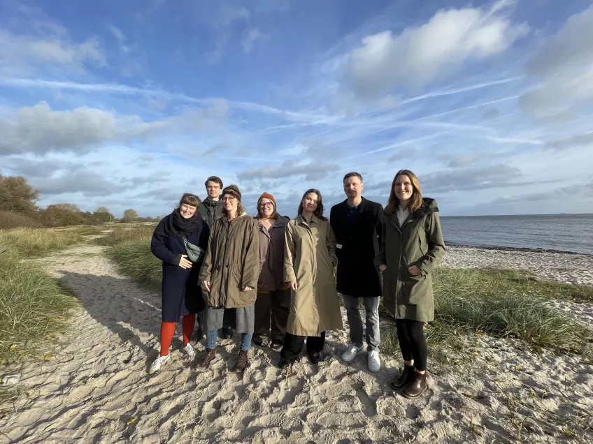 Grupp människor står på en sandstrand.