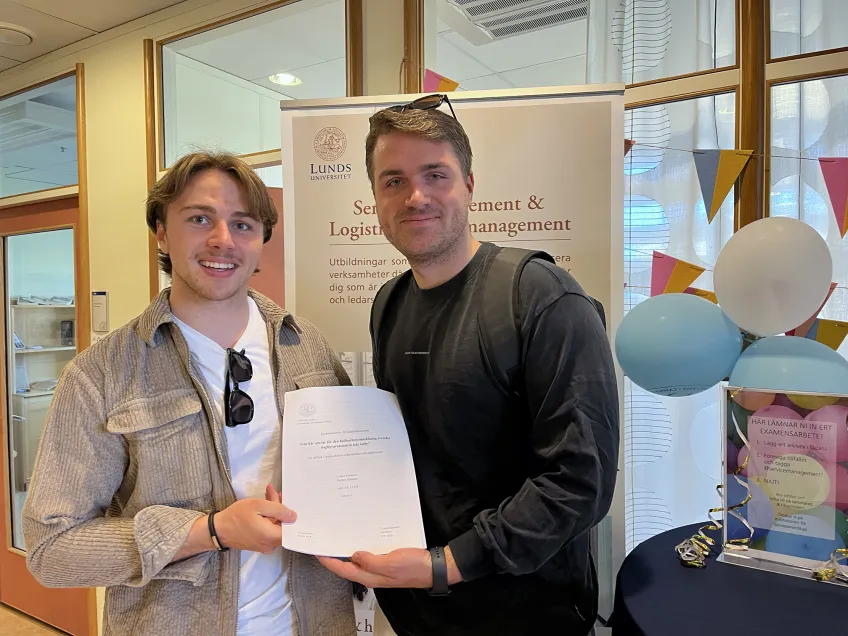 Två studenter som håller i sin uppsats.