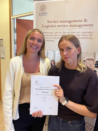 Två studenter som håller i sin uppsats.