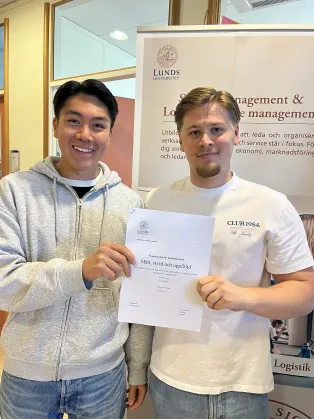 Två studenter som håller i sin uppsats.